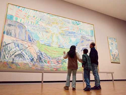 En mor, sønn og far står og ser på Solen av Edvard Munch. De står med ryggen mot kameraet. Fotografi