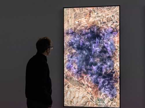 Kunstneren Lawrence Abu Hamdan står i et mørkt rom og ser på en lodrett skjerm som viser en visualisering av støyen 31 vindturbiner vil skape på Golanhøydene. På skjermen ser du at støyen sprer seg utover et stort område som lilla og svart gnistrende røyk. Fotografi