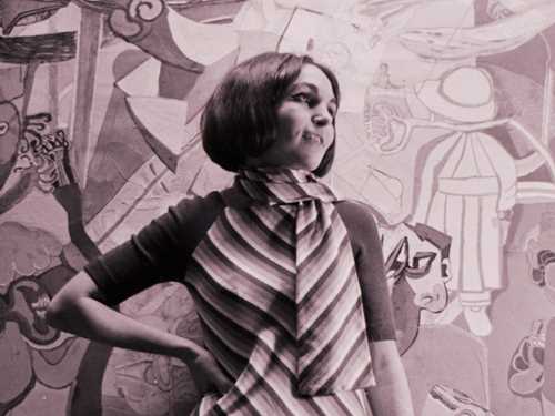 Bilde av en ung kvinne (Paula Rego) i sort hvitt. Hun har på seg en stripete kjole, og har plassert høyre hånd på hoften mens hun ser til siden.