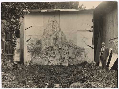 Munch’s open-air studio at Ekely. Edvard Munch is seen on the right side of the image, standing in front of the painting The Human Mountain. Photograph.
