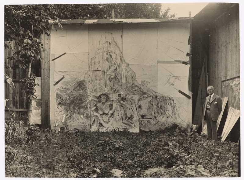 Munchs friluftsatelier på Ekely. Vi ser Edvard Munch til høyre i bildet. Han står foran maleriet Menneskeberget. Fotografi