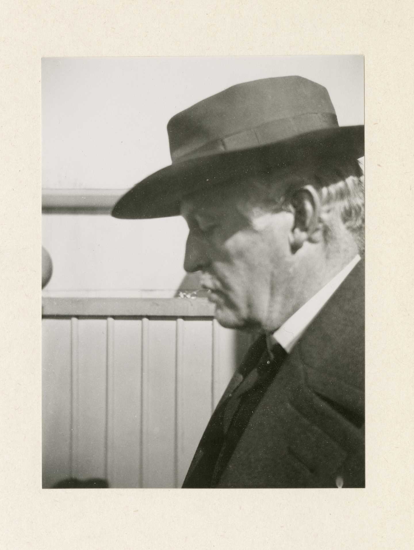 Et svart-hvitt fotografi av Edvard Munchs ansikt i profil. Han har på seg dressjakke, og en mørk hatt som kaster skygge over øynene, som er lukket.