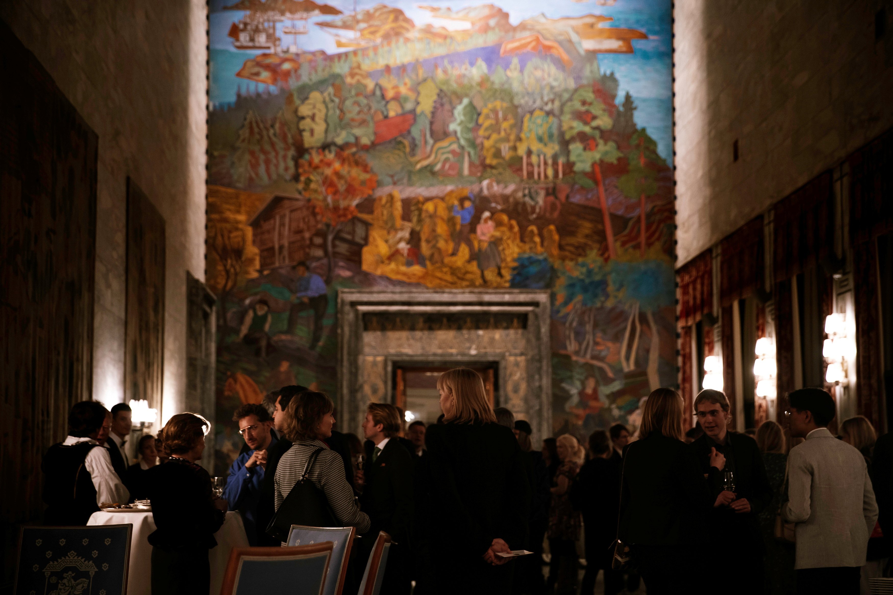 Sal i Oslo Rådhus. Mange mennesker står og snakker sammen og i bakgrunnen ser man et veggmaleri. Fotografi.