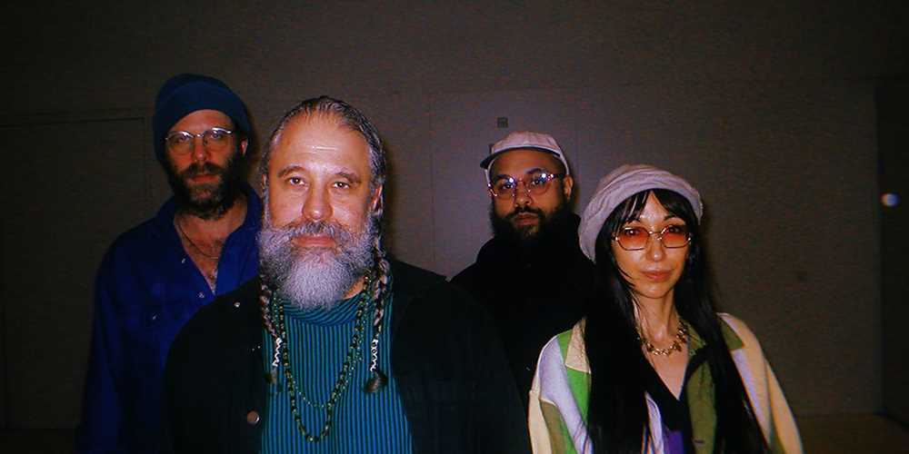 Band photo of three men with beard and one woman with lon hair, sunglasses and a hat. 