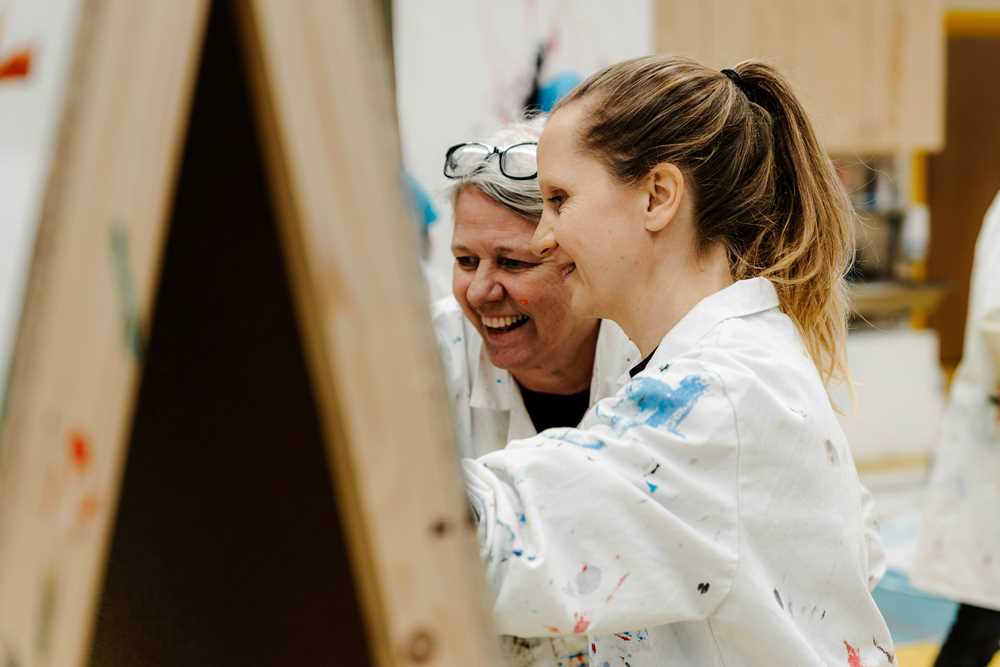 To voksne maler på staffeli.