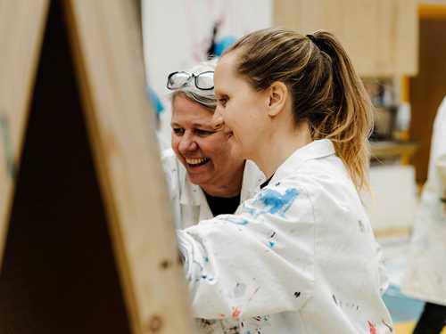 To voksne maler på staffeli.