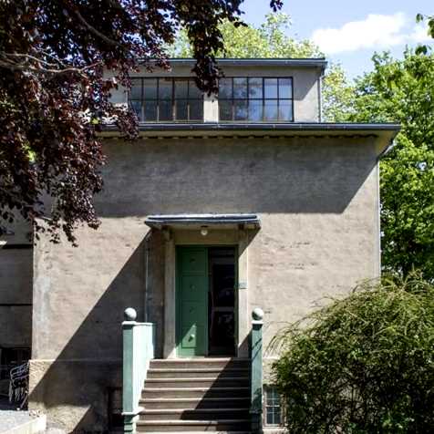 Vinteratelieret på Ekely sett utenfra. En grå murbyggning med en trapp opp mot en grønn inngangsdør.