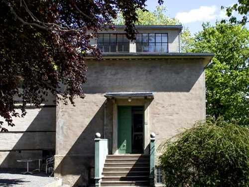 Vinteratelieret på Ekely sett utenfra. En grå murbyggning med en trapp opp mot en grønn inngangsdør.