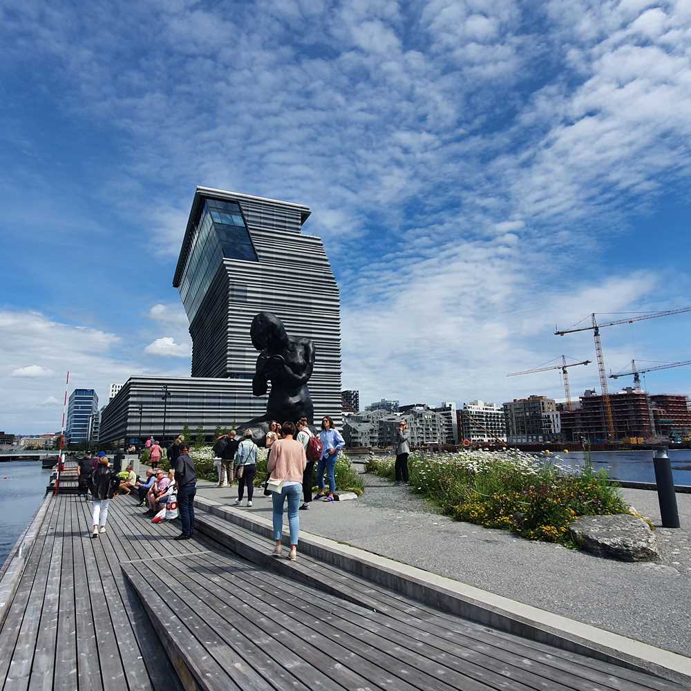 A wide shot of the museum, with the sculpture The Mother in front, a handfull of people standing by.