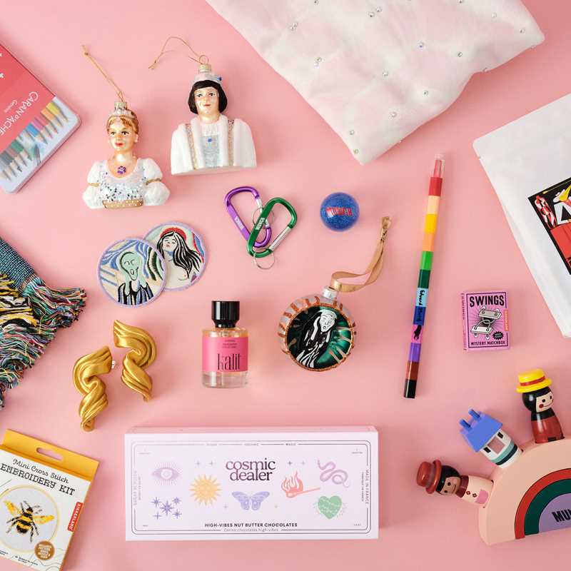 A selection of products from the MUNCH shop, including Cinderella and prince Christmas ornaments, crayons, a Scream ornament, earrings, perfume, a T-shirt with glittering stones, a wooden toy and a bag of coffee. Photograph.