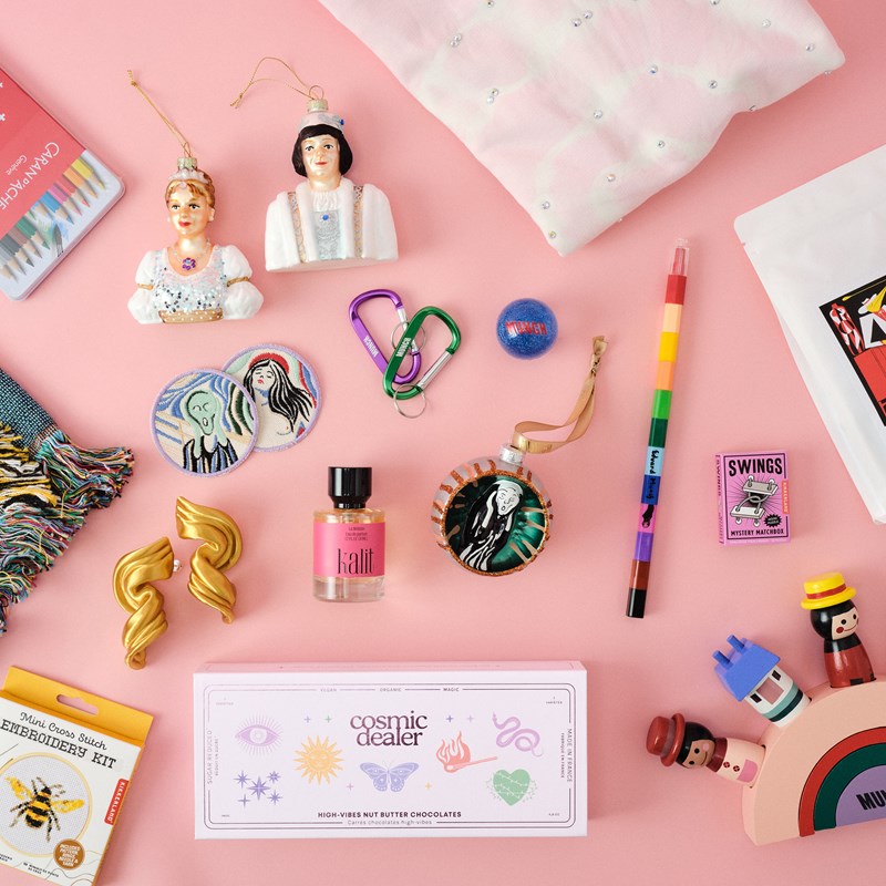 A selection of products from the MUNCH shop, including Cinderella and prince Christmas ornaments, crayons, a Scream ornament, earrings, perfume, a T-shirt with glittering stones, a wooden toy and a bag of coffee. Photograph.