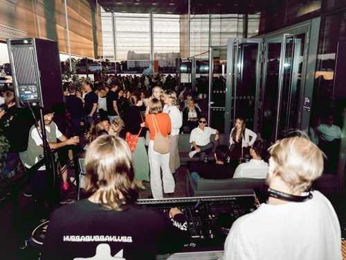 Bakhodene til to DJer skuer ut over menneskemengde på uteservering i kveldssol.