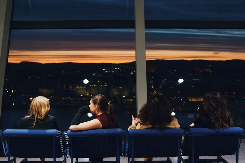 Four girls with their backs to the camera looking out over Oslo at sunset. Photograph.