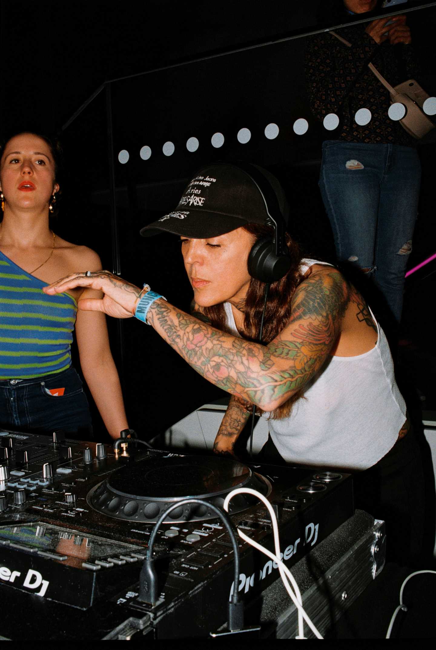 En DJ med headset står bak en miksepult og snurrer plater. Fotografi