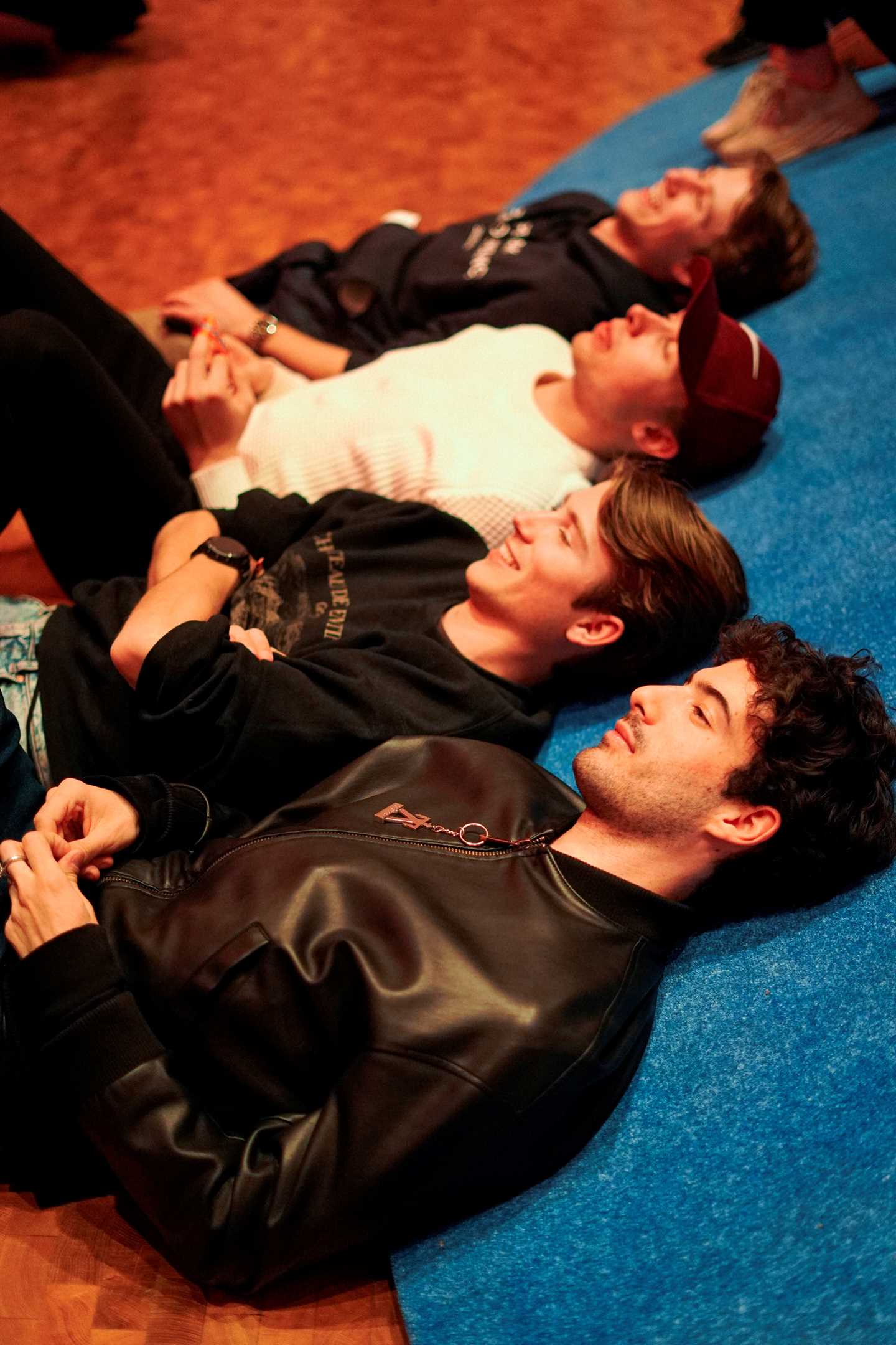 Fire gutter ligger på gulvet, lent opp mot en slak skråning kledd i blått stoff. Fotografi