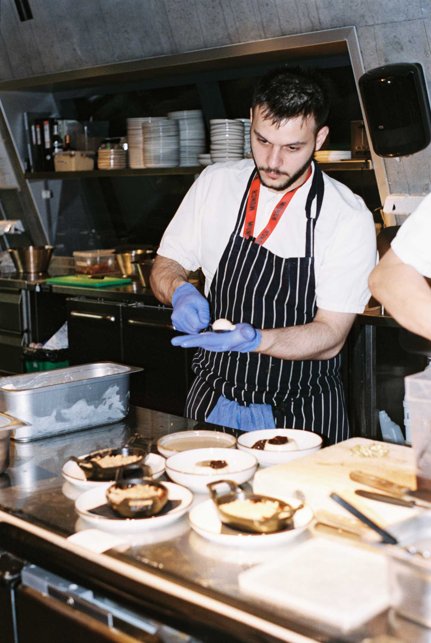 En kokk med stripete forkle og blå plasthansker former avlange kuler med iskrem i hånden sin. Fotografi