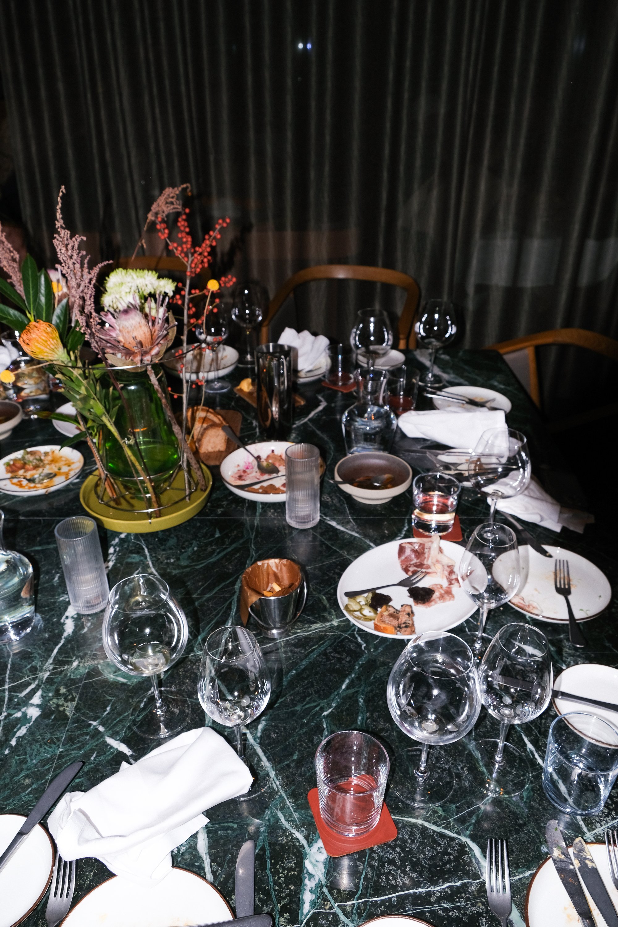 Et forlatt restaurantbord der brukte glass og tallerkner står igjen sammen med brukte servietter og stoler som er skjøvet ut fra bordet. Fotografi