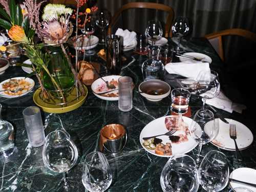 Et forlatt restaurantbord der brukte glass og tallerkner står igjen sammen med brukte servietter og stoler som er skjøvet ut fra bordet. Fotografi