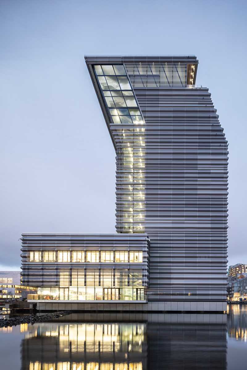 The MUNCH building seen from the south side. A grey structure with illuminated windows and a distinctive bend, making it lean towards the rest of the city. Photograph.
