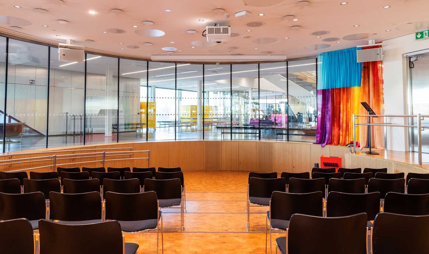 The amphitheatre at MUNCH seen from the back row. Four rows of black chairs are positioned on each side of a central aisle. Photograph.