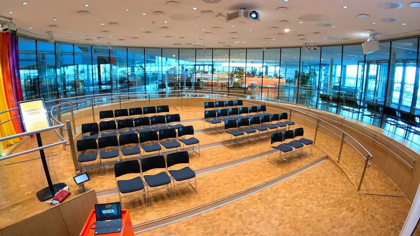 The Amfi hall at MUNCH. A circular room with windows all around. In the middle are four rows of chairs. Photograph.