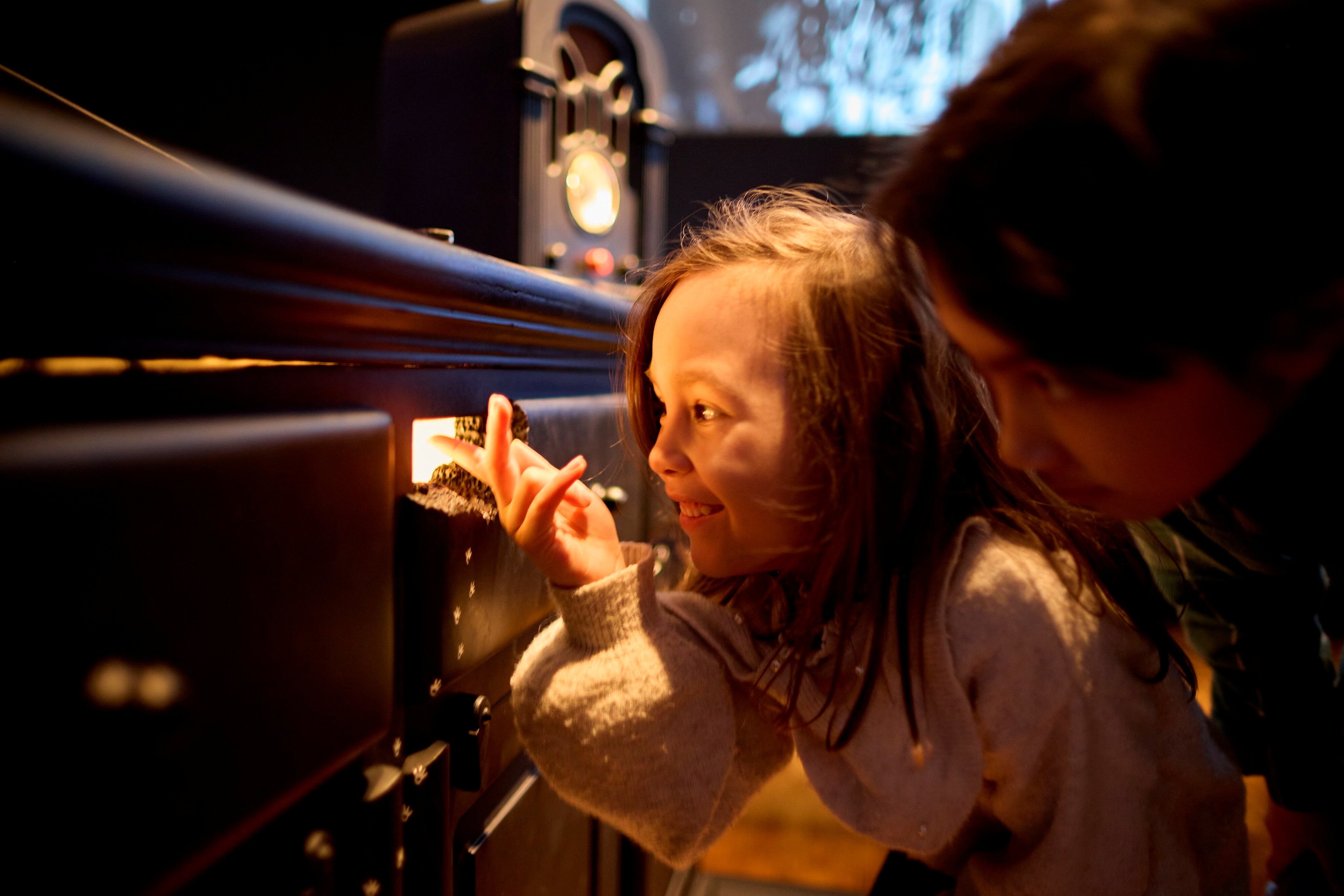 To barn huker seg ned og ser inn gjennom et musehull som det kommer lys ut av. Fotografi