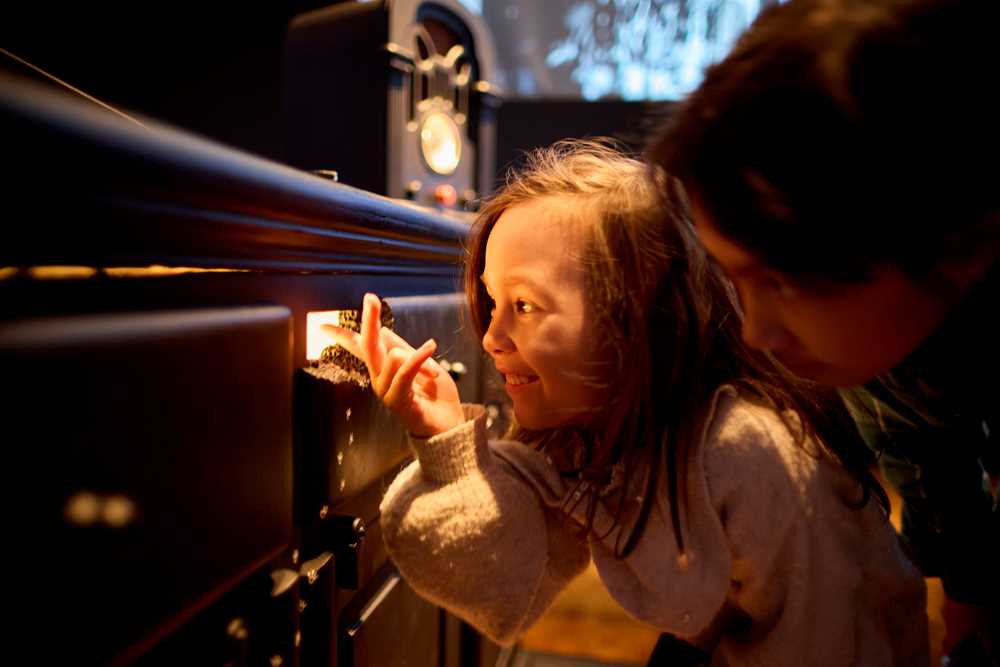 Two children crouch and look through a mouse hole with light coming out of it. Photograph.