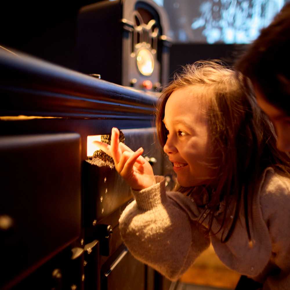 To barn huker seg ned og ser inn gjennom et musehull som det kommer lys ut av. Fotografi