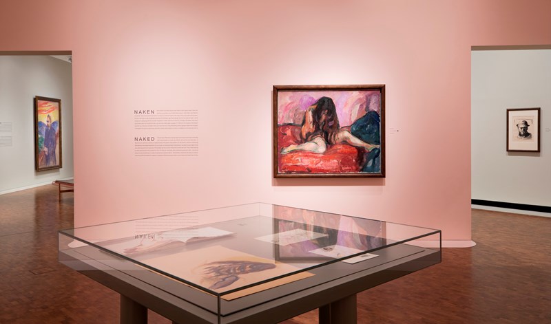 Et glasmonter med tegninger i en av salene i ustillingen Uendelig. I bakgrunnen ser man en rosa vegg der maleriet Gråtende akt av Edvard Munch henger. Fotografi.