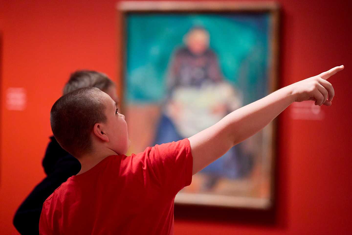 En ung gutt peker på et kunstverk i utstillingen Uendelig mens han snakker med en annen ung gutt. Fotografi