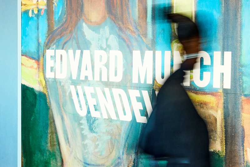 A person walking past the sign at the entrance to the Infinity exhibition at MUNCH. Photograph.