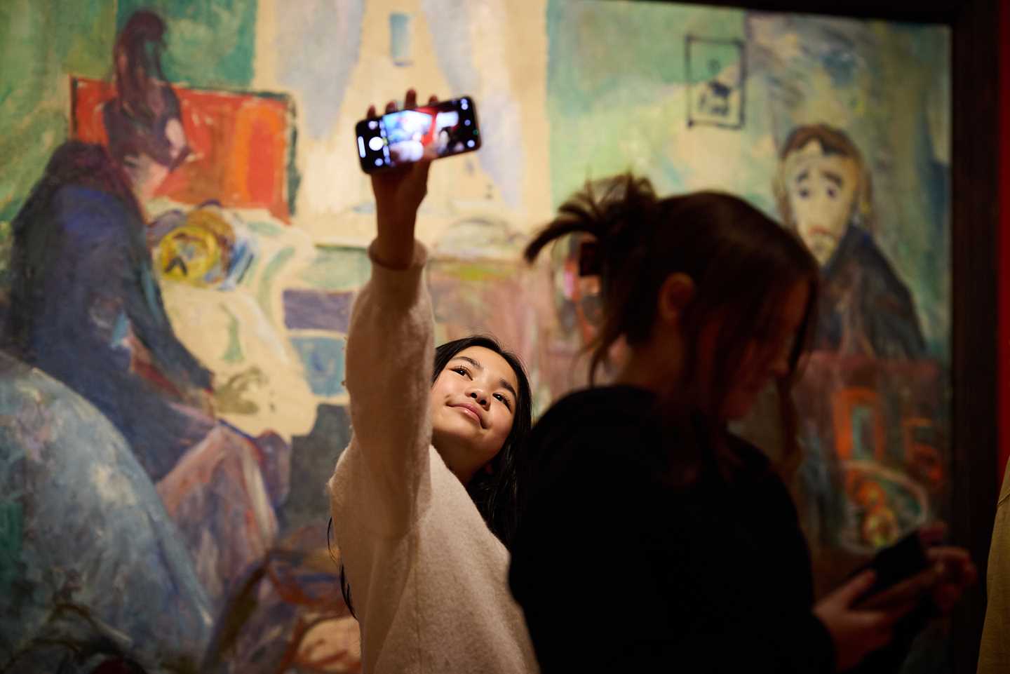 En ung jente tar et bilde av seg selv med mobilen sin foran et maleri av Edvard Munch i utstillingen Uendelig. Fotografi