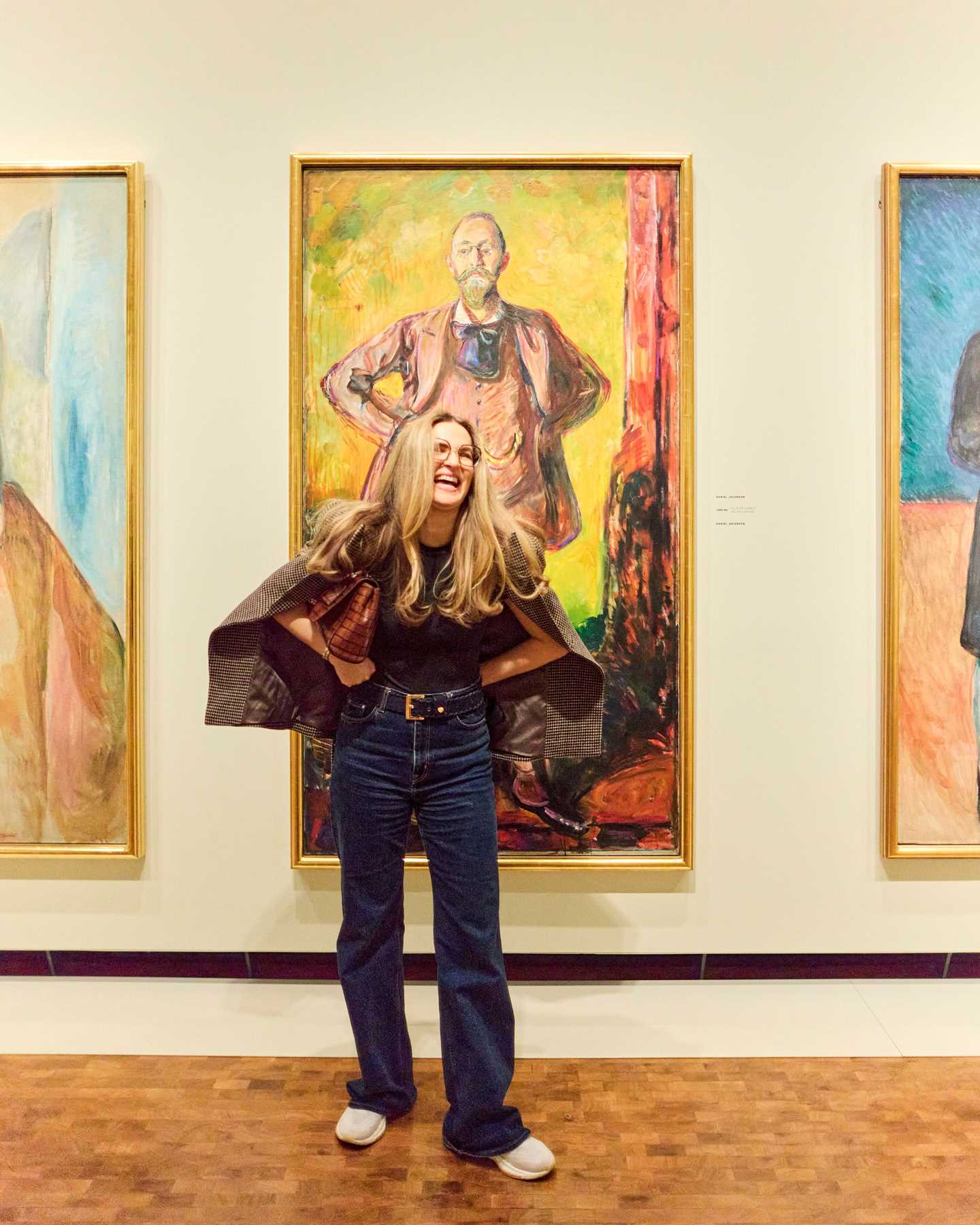 En kvinne poserer foran et maleri av Edvard Munch mens hun ler. Fotografi