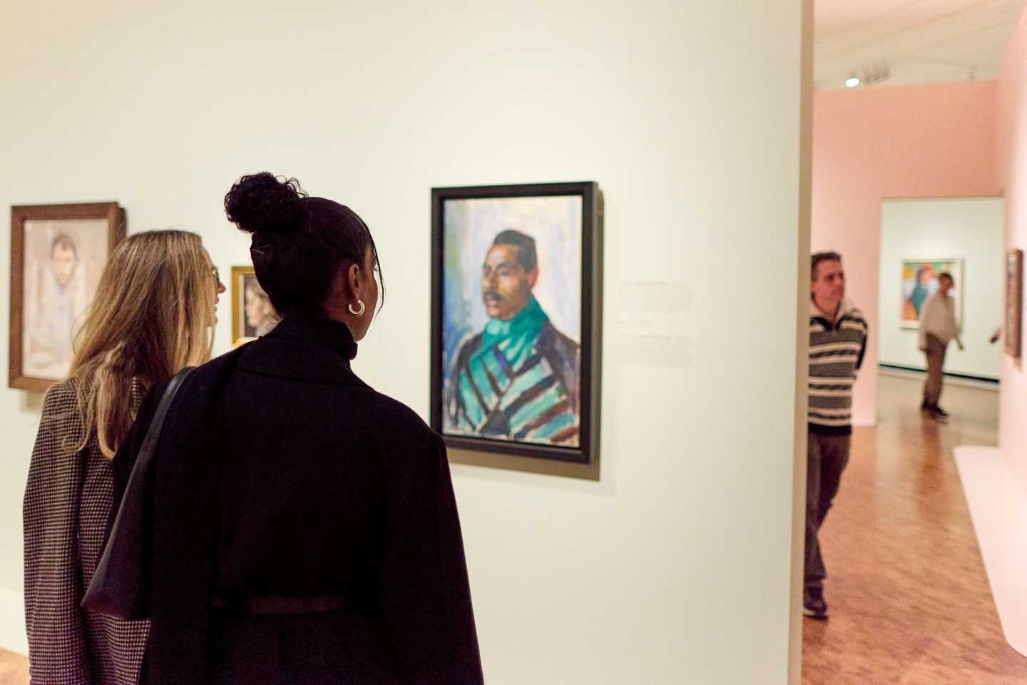 To kvinner står med ryggen mot kameraet og ser på et portrettmaleri malt av Edvard Munch. Fotografi