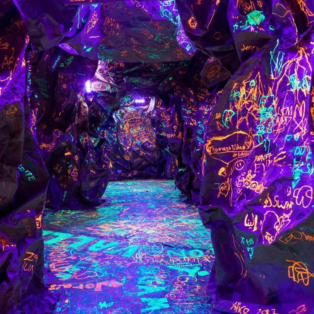 En knudrete, mørk hule der barn og voksne har skriblet med selvlysende blekk. Fotografi