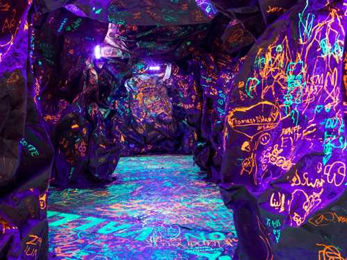 A knobbly, dark cave where children and adults have scribbled with glow-in-the-dark ink. Photograph.