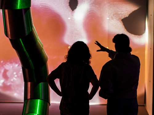 To mennesker står i en utstillingssal og ser på kunst av Sandra Mujinga. Vi ser de bakfra. Fotografi