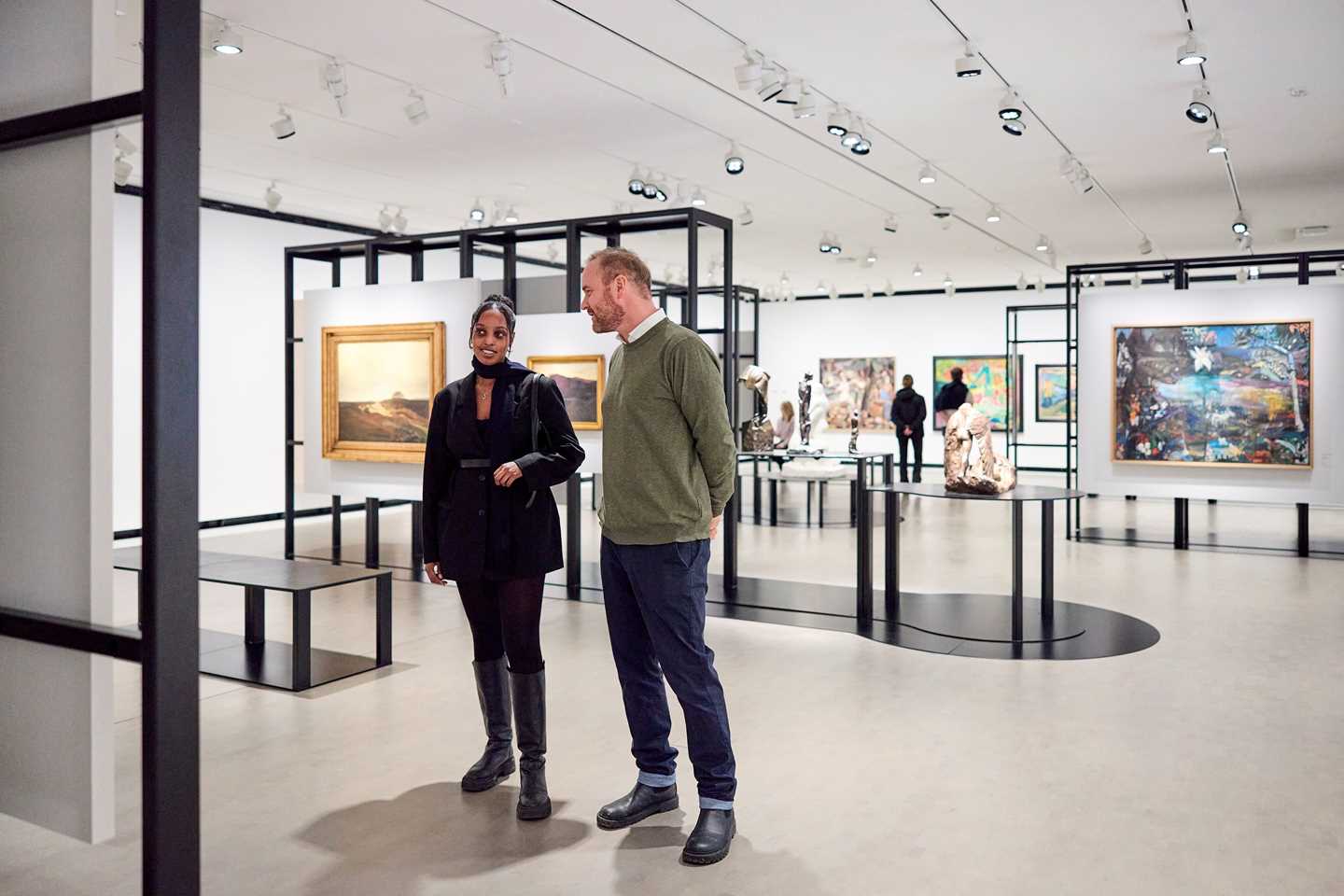 Two people stand in an exhibition room looking at an artwork. Photograph.
