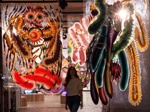 En kvinne går gjennom en gang der malerier henger ned fra taket. Foto