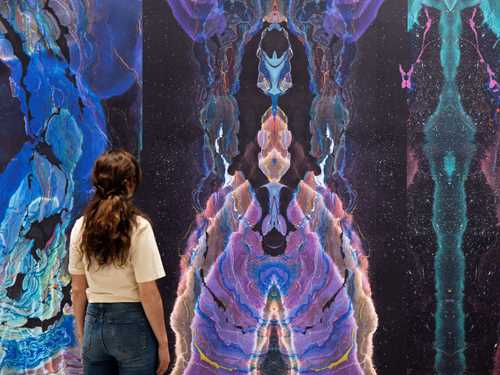 En kvinne står med ryggen til og betrakter en vegg dekket av tapet laget av kunstneren Kerstin Brätsch. Fotografi