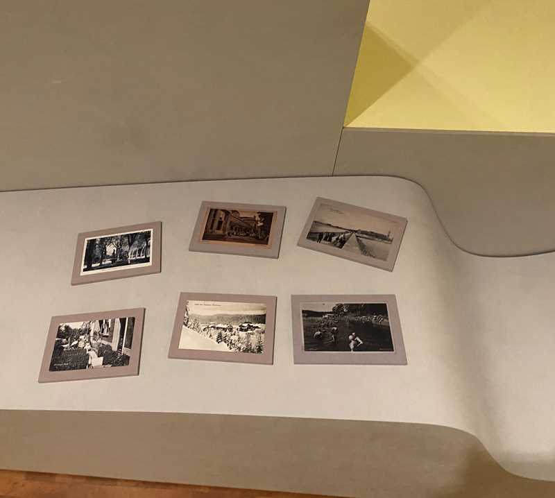 A photograph of six objects placed on moulded furniture within the exhibition space. The objects are reproductions of vintage postcards on small handheld boards. The postcards show different spas, seaside resorts and other destinations in Europe connected to health and wellbeing.