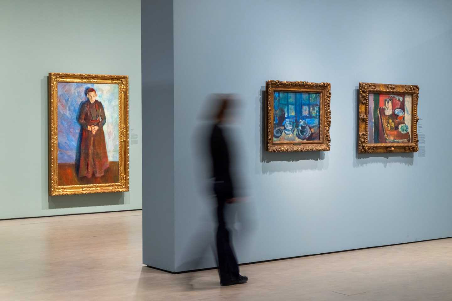 Bilde fra utstillingssal med en person som går mot verkene Det blå kjøkken og Det røde kjøkken av Ludvig Karsten. Fotografi