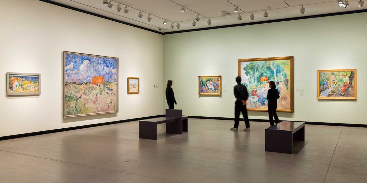 Tre mennesker står i en utstillingssal og ser på verk av Ludvig Karsten. Fotografi