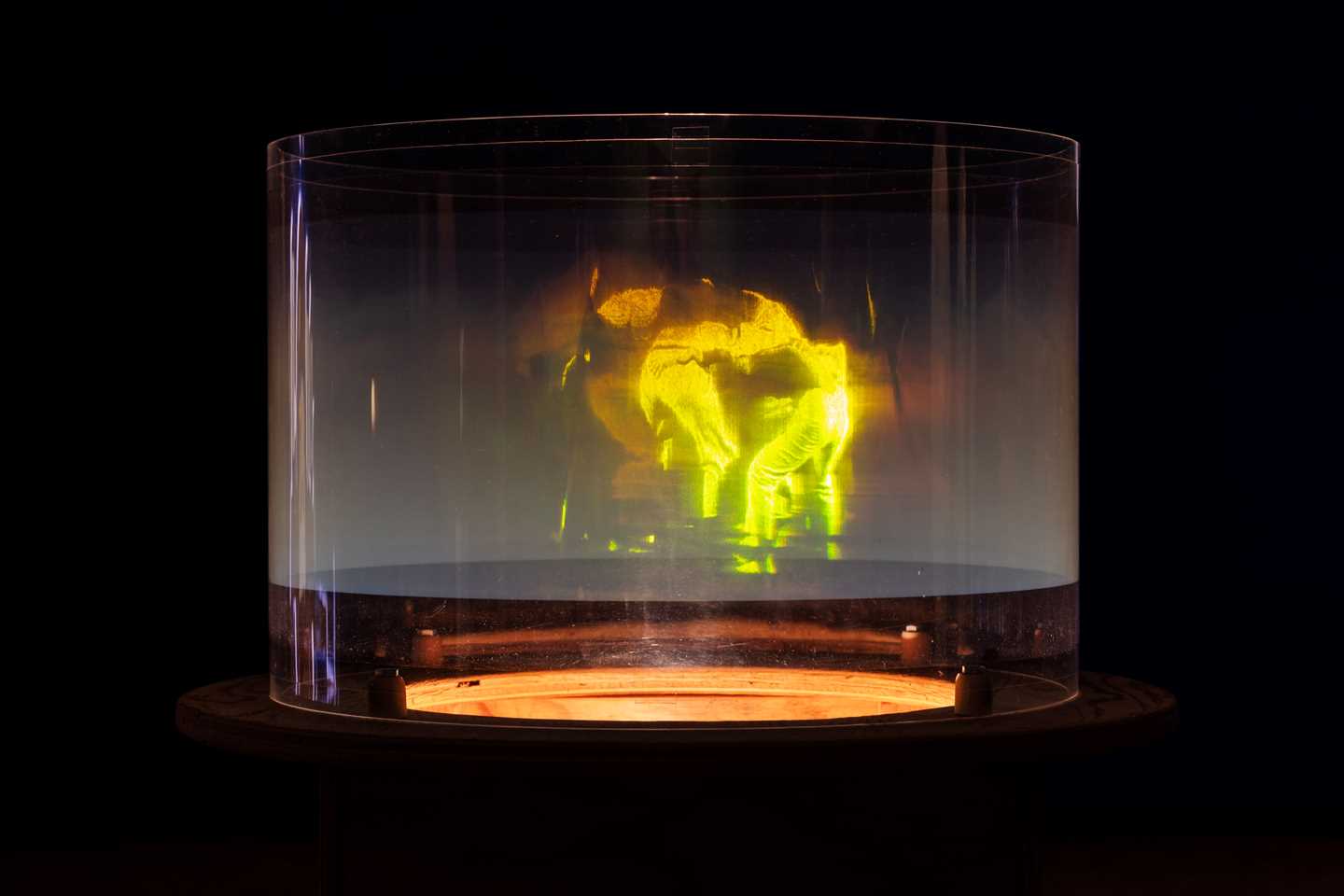 Et hologram viser mennesker som danser sammen i en ring. Menneskene er grønne og lyser opp bildet som ellers er helt mørkt. Fotografi