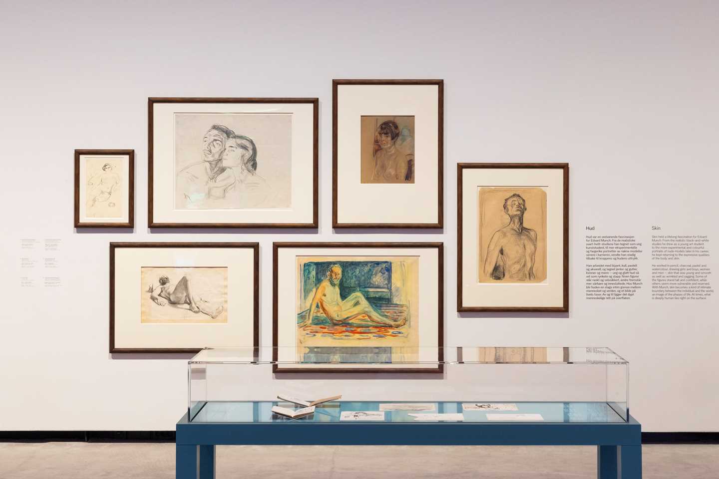 Seks innrammede tegninger av Edvard Munch henger på en vegg. Foran står et glassmonter som viser noen av Edvard Munchs skissebøker. Fotografi