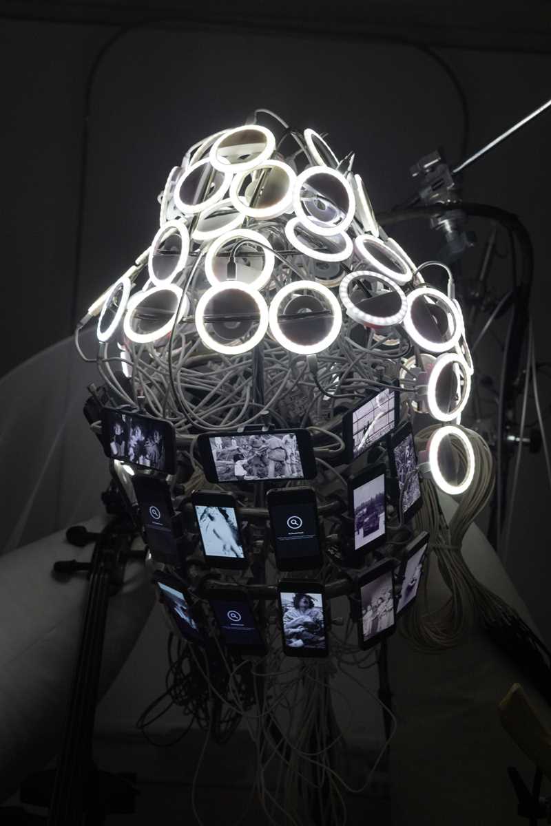 Sirkler av lysdioder med hvitt lys, ledninger og mobilskjermer er satt sammen slik at det har samme form som et Buddha-hode. Dette er et nærbilde av en del av installasjonen. Fotografi