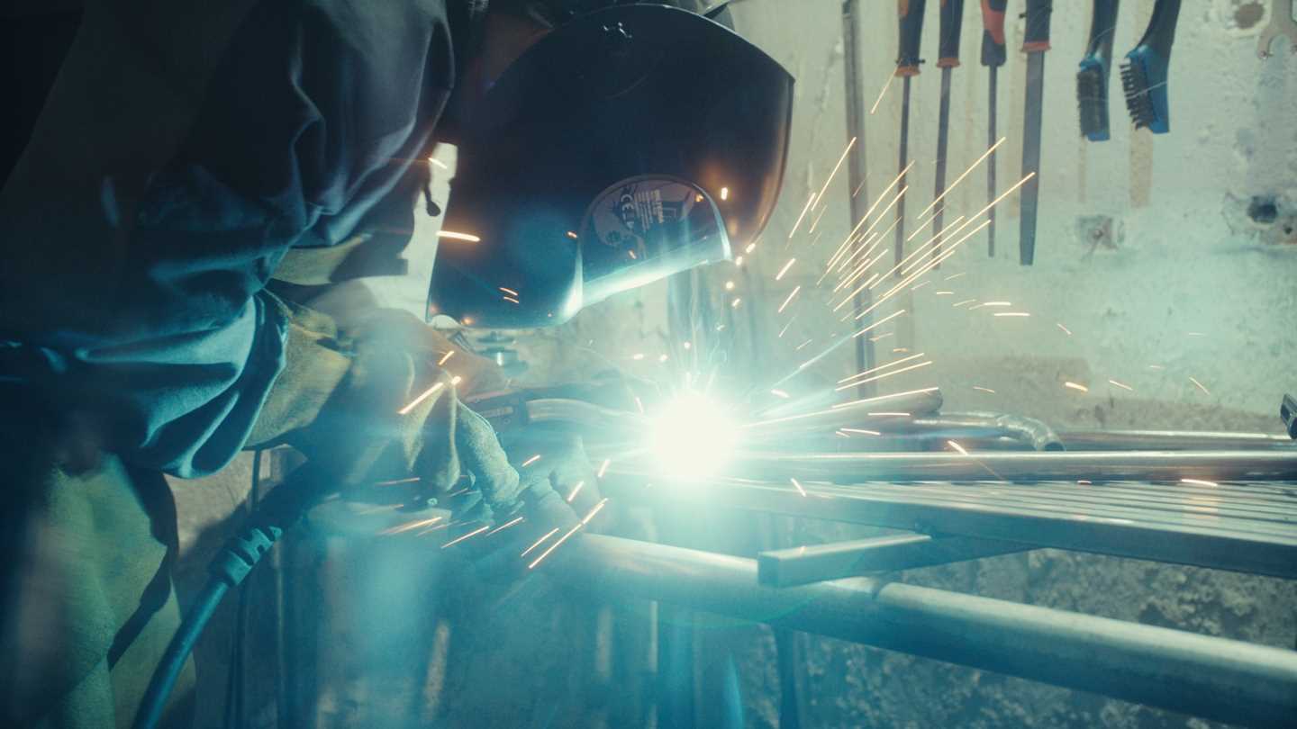 Kunstneren Kim Hankyul står bøyd over en arbeidsbenk der han sveiser metall. Han har på seg beskyttelsesvisir og det er skarpt lys og gnistregn rundt ansiktet hans. Fotografi
