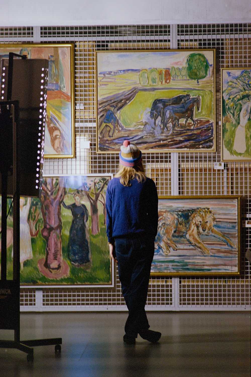 Artist Marie Ulven is standing with her back towards the camera in front of several works of Edvard Munch. Photography