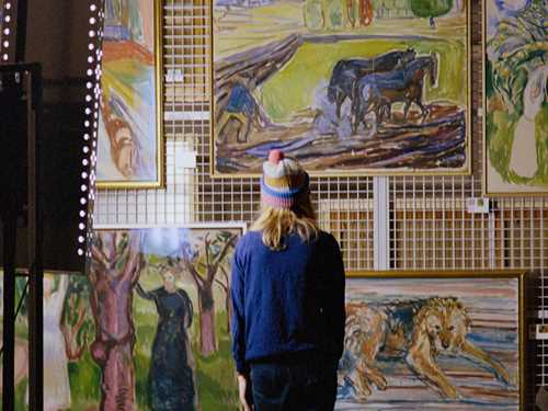 Artist Marie Ulven is standing with her back towards the camera in front of several works of Edvard Munch. Photography