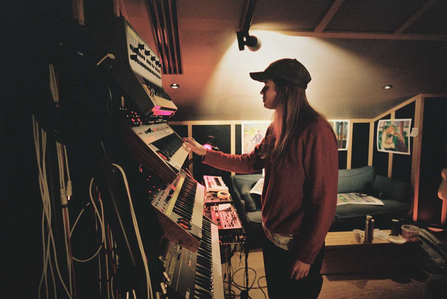 Artist Marie Ulven is standing beside a wall with several keyboards mounted one below the other. She is playing the keys on one of the keyboards. Photograph.